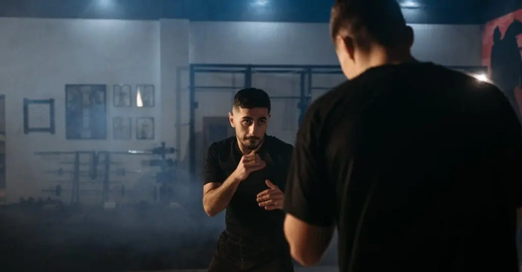 A man in a fighting stance facing an opponent in a dimly lit gym during a practical self defense training for beginners class.