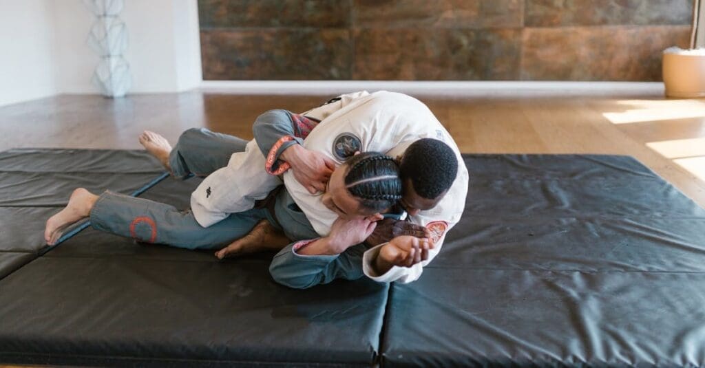 Two martial artists in gis practicing ground control and positioning on a black mat during self defense training for beginners.