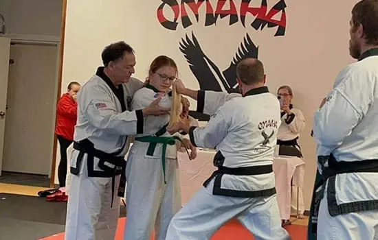 Student practices a board-breaking technique with instructors during beginner martial arts skills training